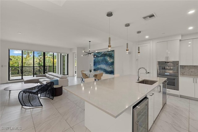 kitchen featuring white cabinets, hanging light fixtures, sink, and beverage cooler