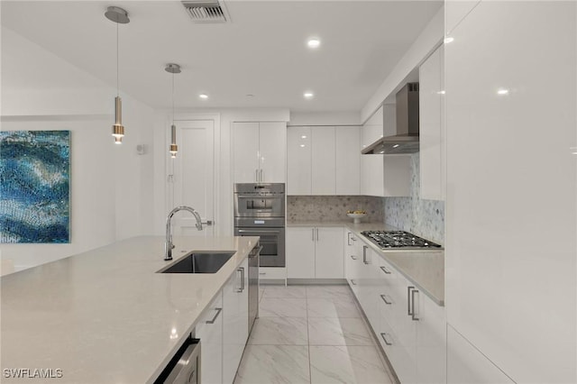 kitchen with decorative light fixtures, white cabinetry, sink, stainless steel appliances, and wall chimney exhaust hood