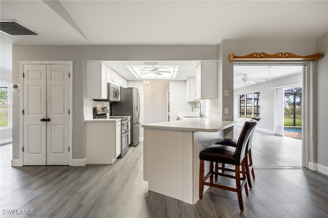 kitchen featuring kitchen peninsula, stainless steel appliances, ceiling fan, sink, and white cabinets