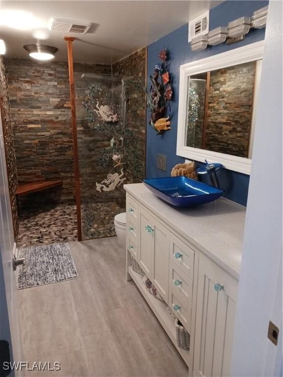 bathroom with toilet, a tile shower, vanity, and hardwood / wood-style flooring