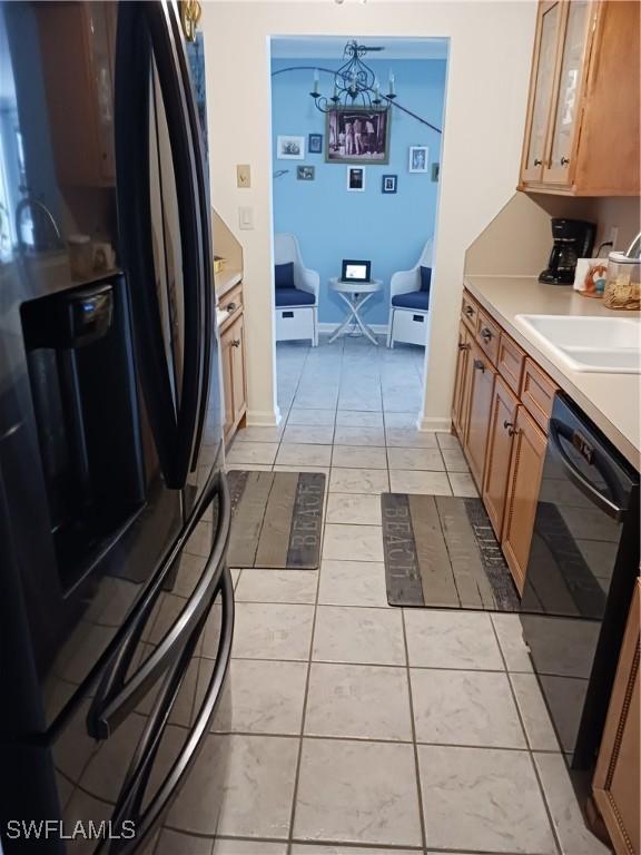 kitchen featuring sink, light tile patterned floors, hanging light fixtures, black appliances, and a notable chandelier