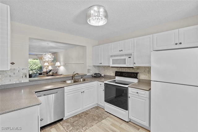 kitchen featuring white appliances, sink, pendant lighting, white cabinets, and a chandelier