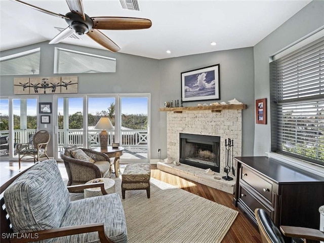 living room featuring hardwood / wood-style flooring, ceiling fan, and a stone fireplace