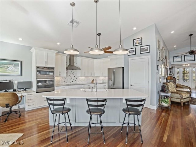 kitchen with appliances with stainless steel finishes, wall chimney exhaust hood, pendant lighting, white cabinets, and lofted ceiling