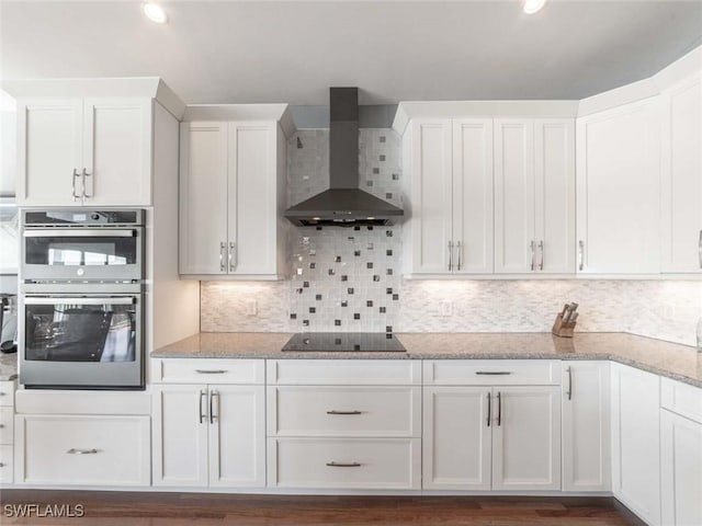 kitchen with white cabinets, wall chimney exhaust hood, black electric cooktop, and double oven