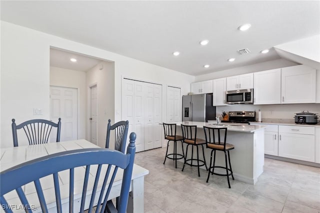 kitchen featuring a kitchen breakfast bar, white cabinetry, an island with sink, and appliances with stainless steel finishes