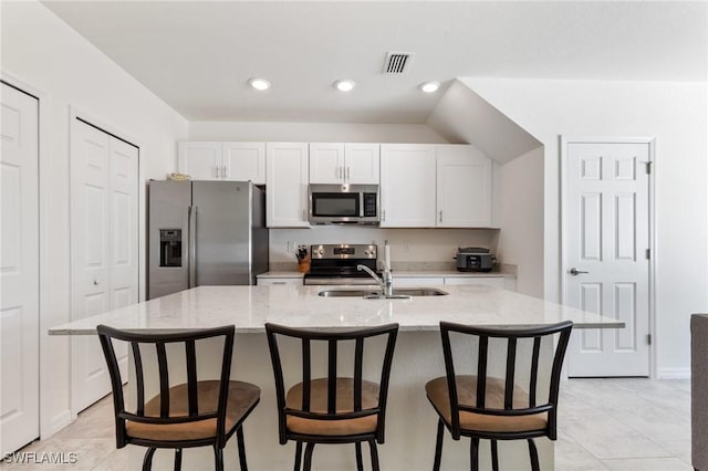 kitchen with light stone countertops, appliances with stainless steel finishes, sink, a center island with sink, and white cabinets