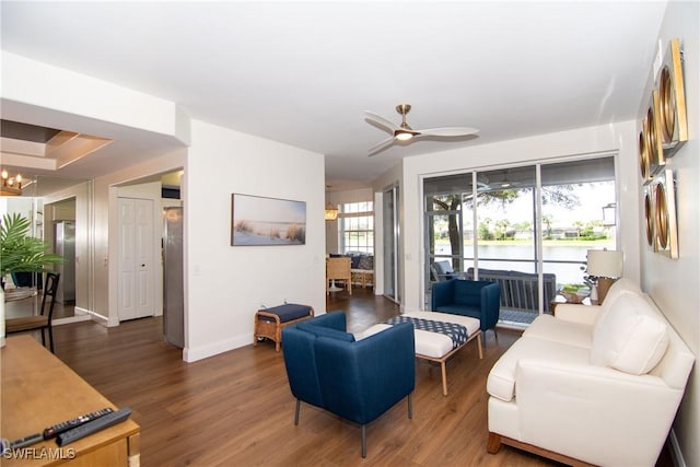 living room with ceiling fan with notable chandelier, dark wood-style flooring, a water view, and baseboards