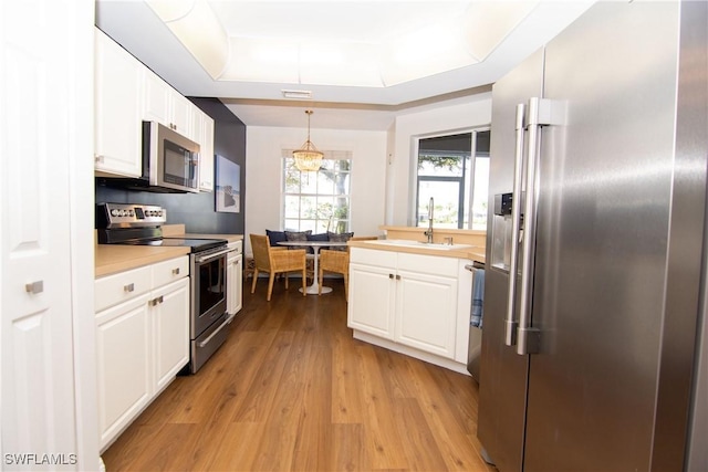 kitchen featuring appliances with stainless steel finishes, sink, pendant lighting, white cabinets, and light hardwood / wood-style floors