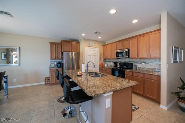 kitchen featuring appliances with stainless steel finishes, a breakfast bar, sink, light tile patterned floors, and an island with sink