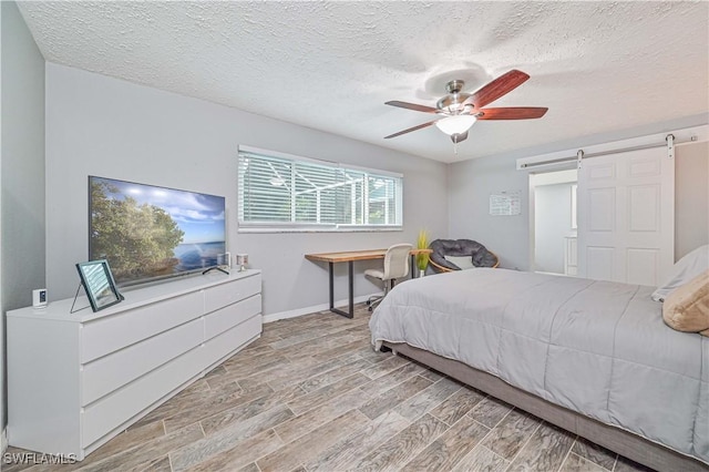 bedroom with ceiling fan, a barn door, light wood-type flooring, and a textured ceiling