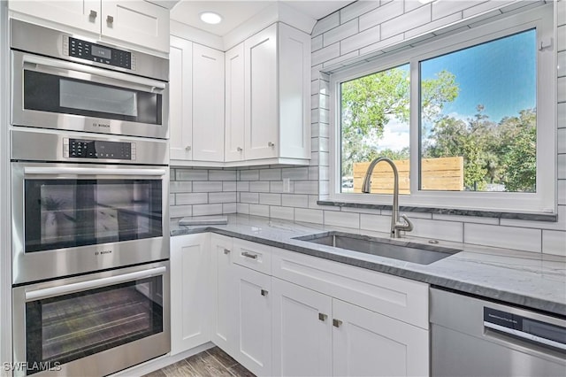 kitchen with white cabinets, appliances with stainless steel finishes, sink, and light stone counters