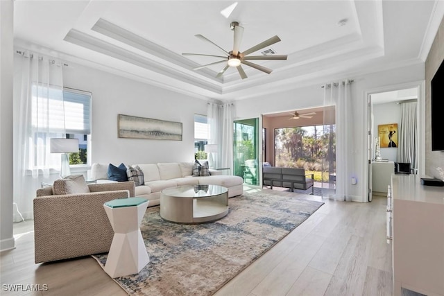 living room with a tray ceiling, a healthy amount of sunlight, and light wood-type flooring