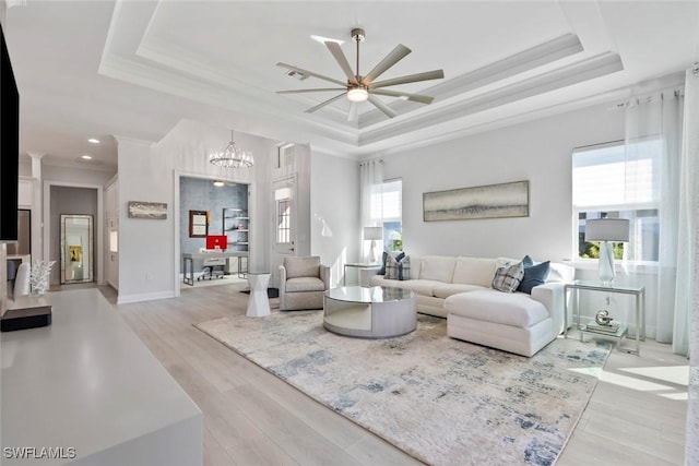 living room featuring ceiling fan with notable chandelier, light wood-type flooring, a raised ceiling, and ornamental molding