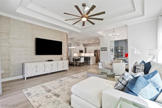 living room featuring ceiling fan with notable chandelier, light hardwood / wood-style floors, crown molding, and a tray ceiling