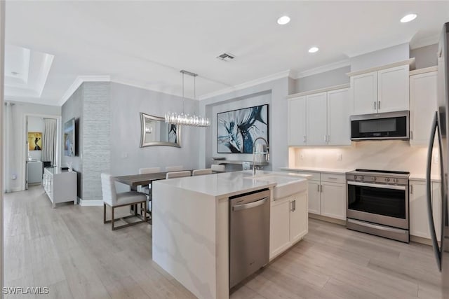 kitchen featuring a kitchen island with sink, sink, light wood-type flooring, decorative light fixtures, and stainless steel appliances