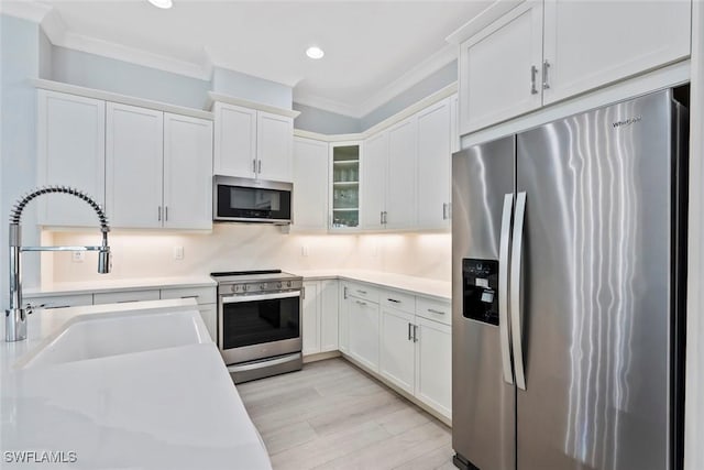 kitchen featuring decorative backsplash, ornamental molding, stainless steel appliances, sink, and white cabinetry