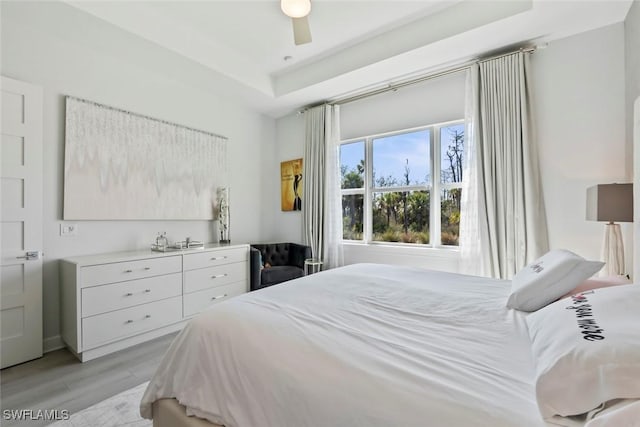 bedroom featuring ceiling fan, a raised ceiling, and light wood-type flooring