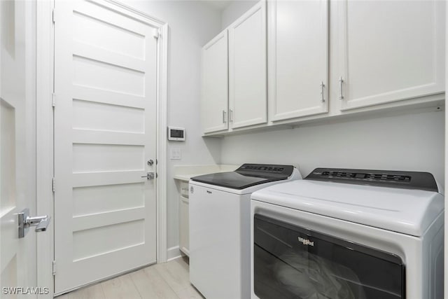 laundry area with light hardwood / wood-style floors, cabinets, and washing machine and clothes dryer