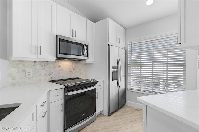 kitchen featuring light stone countertops, light wood-type flooring, appliances with stainless steel finishes, tasteful backsplash, and white cabinetry