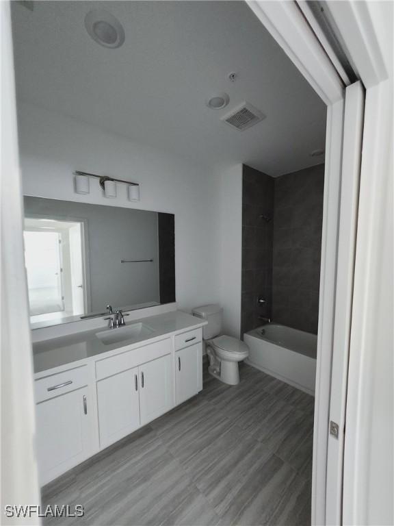 full bathroom featuring vanity, tiled shower / bath combo, hardwood / wood-style flooring, and toilet