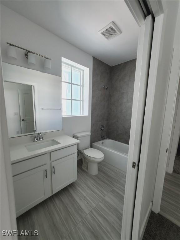 full bathroom with hardwood / wood-style flooring, vanity, tiled shower / bath combo, and toilet