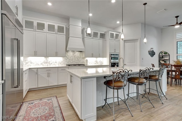 kitchen with white cabinets, ceiling fan, premium range hood, and a kitchen island with sink