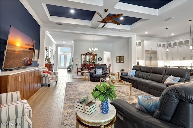 living room featuring ornamental molding, ceiling fan with notable chandelier, light hardwood / wood-style flooring, and coffered ceiling