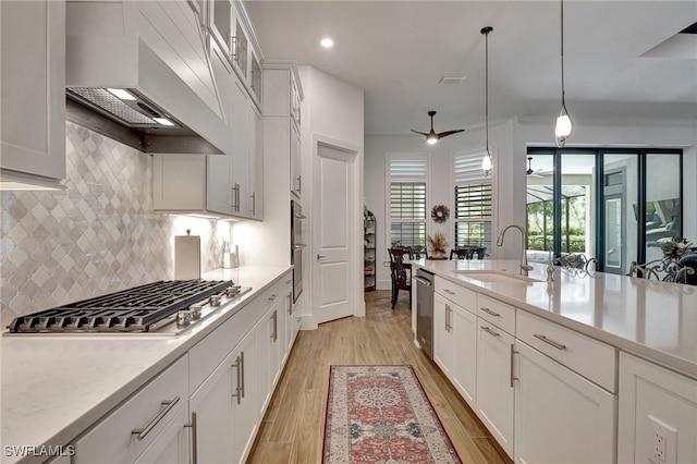 kitchen with appliances with stainless steel finishes, custom exhaust hood, sink, decorative light fixtures, and white cabinetry