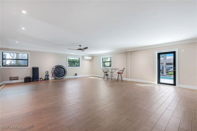 unfurnished living room with a wall mounted AC, ceiling fan, crown molding, and light hardwood / wood-style floors