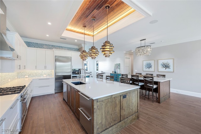 kitchen featuring white cabinets, high end appliances, hanging light fixtures, and an island with sink