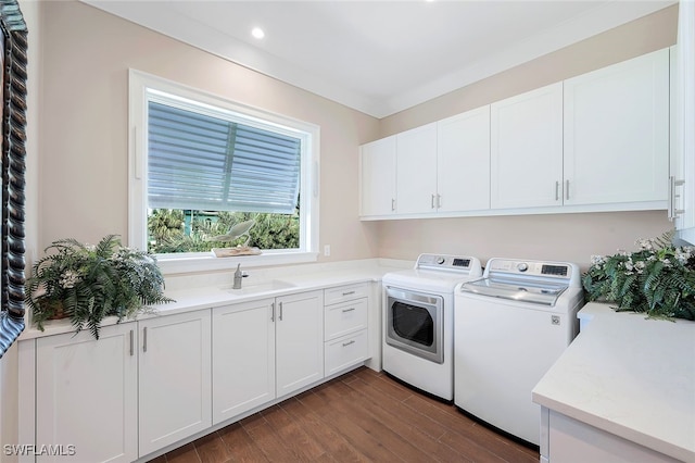 clothes washing area with dark wood-type flooring, sink, cabinets, ornamental molding, and washer and clothes dryer