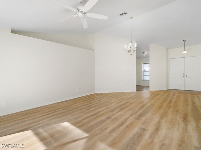 spare room with ceiling fan with notable chandelier, light hardwood / wood-style floors, and lofted ceiling