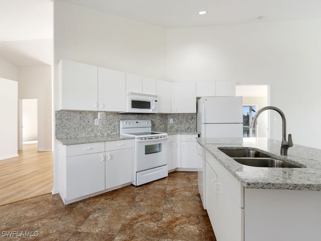 kitchen featuring white cabinetry, white appliances, sink, and a towering ceiling