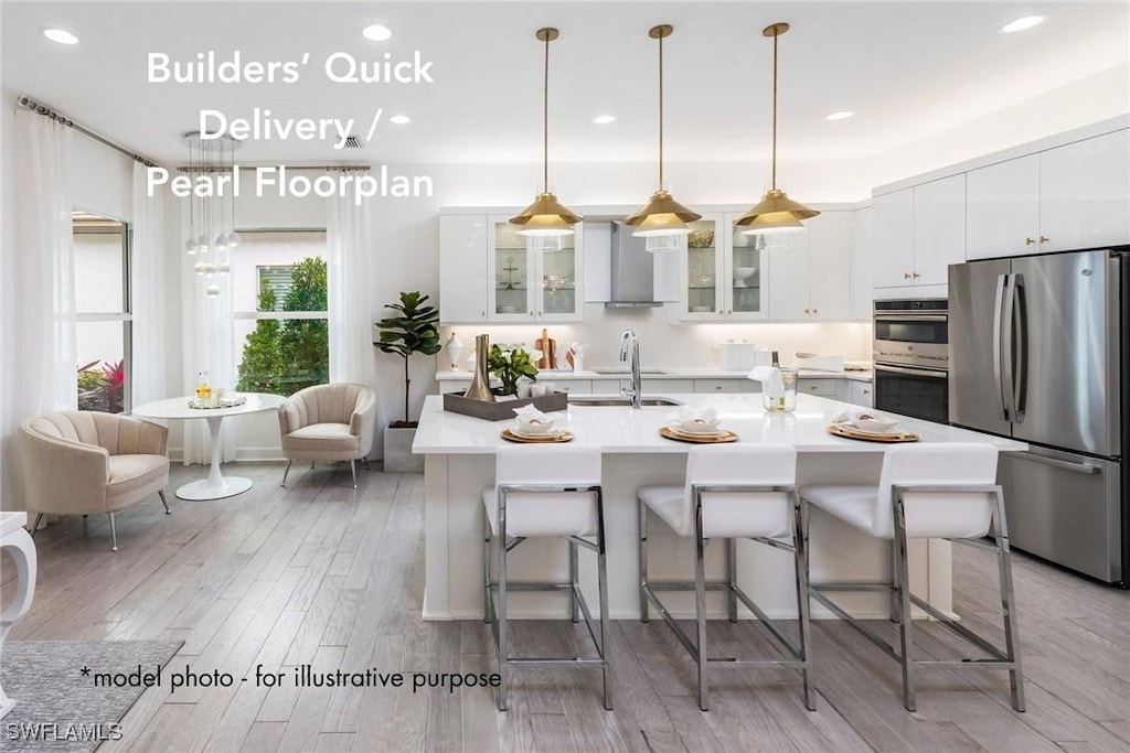 kitchen featuring a breakfast bar area, light hardwood / wood-style flooring, stainless steel appliances, and wall chimney range hood