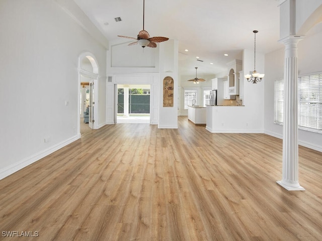 unfurnished living room with decorative columns, light hardwood / wood-style floors, ceiling fan with notable chandelier, and high vaulted ceiling