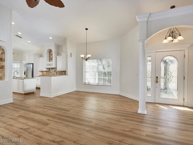 foyer entrance featuring arched walkways, plenty of natural light, light wood-style flooring, and ceiling fan with notable chandelier