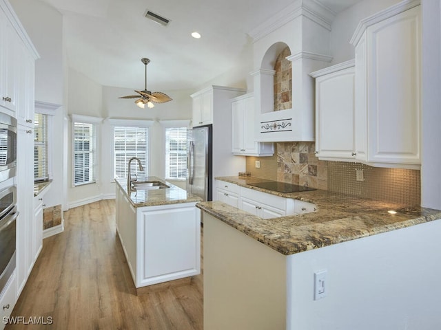 kitchen featuring a peninsula, a sink, appliances with stainless steel finishes, an island with sink, and dark stone countertops