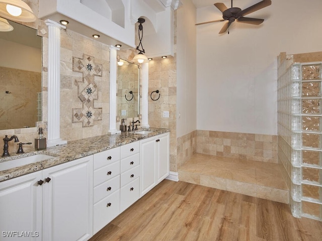 full bath with double vanity, a ceiling fan, a sink, and wood finished floors