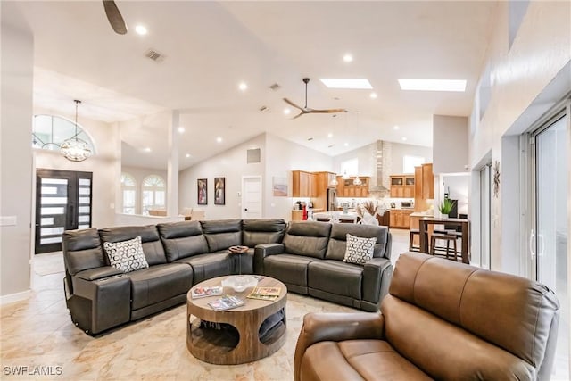 living room featuring ceiling fan with notable chandelier, high vaulted ceiling, and a skylight