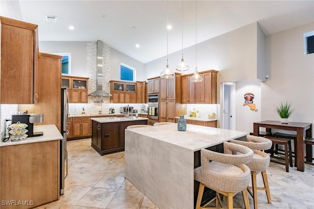 kitchen featuring pendant lighting, a center island, a kitchen bar, wall chimney range hood, and backsplash