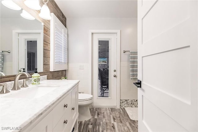 bathroom with hardwood / wood-style flooring, tile walls, toilet, and vanity