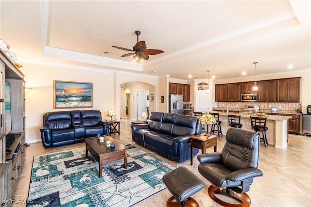 tiled living room with ceiling fan, ornamental molding, and a tray ceiling