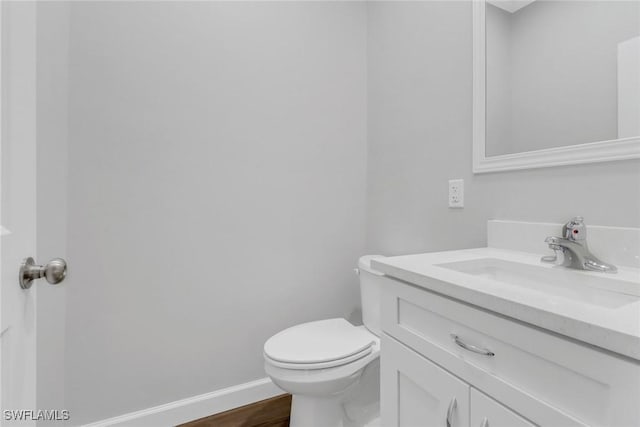 half bath featuring toilet, wood finished floors, vanity, and baseboards