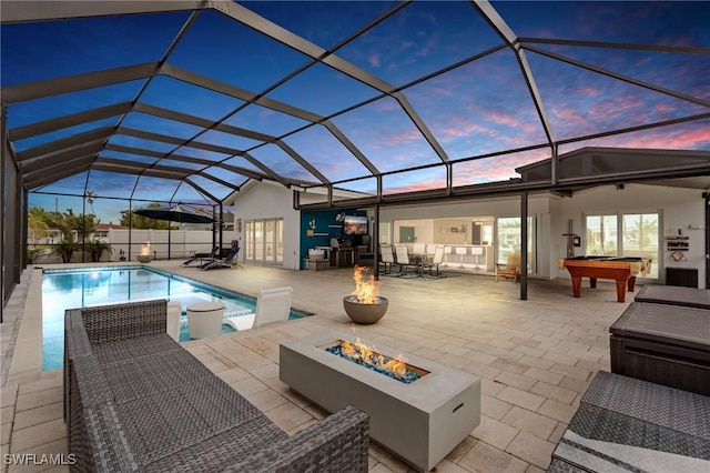 pool at dusk featuring a lanai, an outdoor fire pit, and a patio