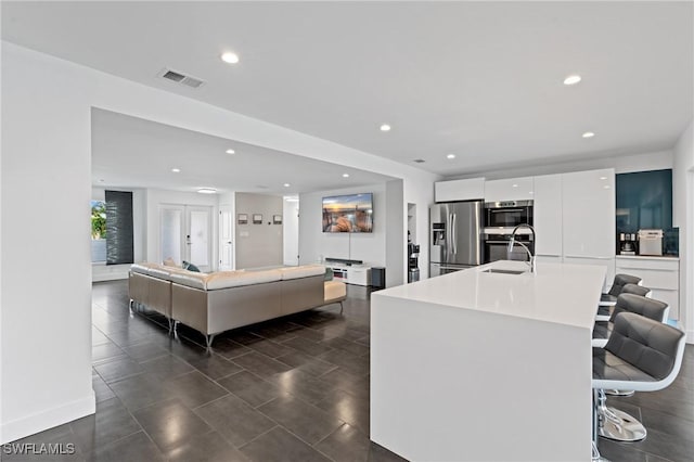 kitchen with stainless steel fridge, a kitchen island with sink, sink, white cabinets, and a breakfast bar area