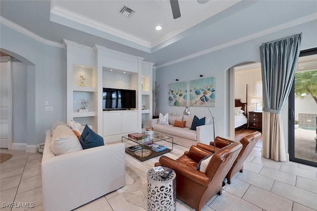 living room featuring ceiling fan, built in shelves, a tray ceiling, and ornamental molding