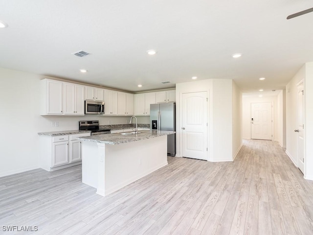 kitchen featuring light stone counters, stainless steel appliances, a center island with sink, light wood-type flooring, and white cabinetry