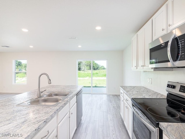 kitchen with stainless steel appliances, sink, white cabinets, light wood-type flooring, and light stone countertops