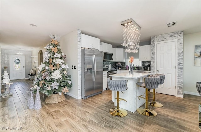 kitchen with light wood-type flooring, tasteful backsplash, stainless steel appliances, white cabinetry, and a breakfast bar area